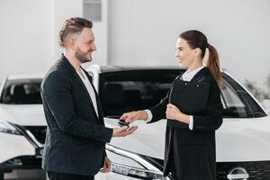 Manager gives a car keys to man in the car dealership. Auto seller and a man who bought a vehicle shake hands. Dealer giving key to new owner in auto show or salon photo