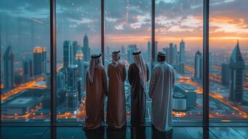 exitoso musulmán empresarios en tradicional blanco atuendo en pie en su moderno oficina mirando fuera de el ventana en grande ciudad con rascacielos exitoso saudita, emirati foto