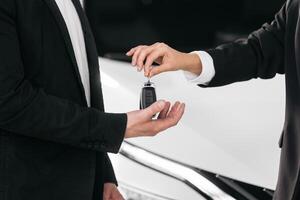 Male hand gives a car keys to female hand in the car dealership close up. Unrecognized auto seller and a man who bought a vehicle shake hands. Dealer giving key to new owner in auto show or salon photo