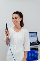 Middle aged beautician holding ultrasound device for face lifting and skin tightening procedure. Young woman cosmetologist using modern cosmetology equipment in clinic photo