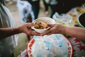 el mano de el vagabundo extiende a recibir comida desde donaciones con voluntarios recogiendo comida foto