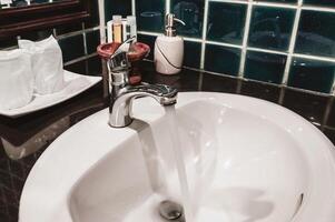 grifo en un blanco lavabo en un baño con azul pared losas foto