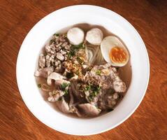 A bowl of noodles, minced pork, meatballs and eggs in a broth topped with coriander and fried garlic. photo