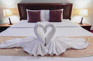 White rattles were rolled together in the shape of a swan and placed on a mattress on a wooden bed with lamps on either side of the bed. photo