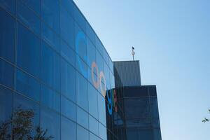 Modern Google office building with reflective facade, flag and tree, clear sky viewed from below. photo