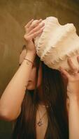 girl posing with big seashell, girl covering face with seashell, vertical video