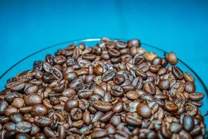 black coffee beans in a transparent glass bowl, on a green table. photo