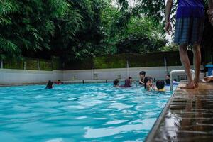 Jepara, Central Java, April 14, 2024 - Swimming pool rides surrounded by trees are full of visitors during holidays. photo