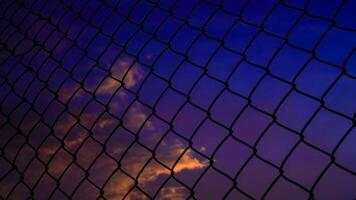 shot of the iron net fence against the background of an orange sky in the afternoon. photo