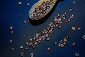 Black coffee beans are seen close up with a wooden spoon on a black cloth. photo