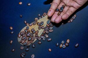 Black coffee beans are seen close up with a wooden spoon on a black cloth. photo