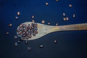 Black coffee beans are seen close up with a wooden spoon on a black cloth. photo