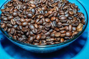 black coffee beans in a transparent glass bowl, on a green table. photo