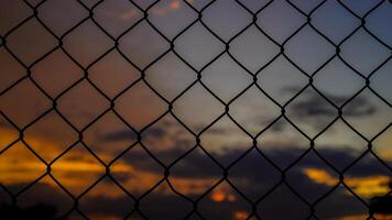 shot of the iron net fence against the background of an orange sky in the afternoon. photo