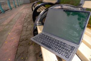laptop tablet with blank screen on park bench. photo