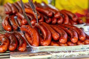 asado Fresco carne de vaca salchichas en un parrilla con alicates foto