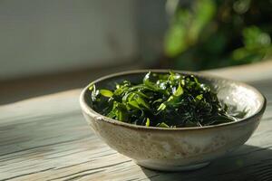 A plate with green salad made from chukka seaweed on a wooden table, illuminated by bright sunlight. Vegan seafood. photo