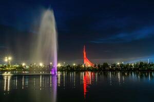 UZBEKISTAN, TASHKENT - SEPTEMBER 15, 2023 Illuminated monument of independence in the form of a stele with a Humo bird and fountain in the New Uzbekistan park at nighttime in autumn. photo