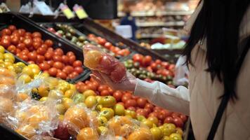 In supermarket, woman selects fresh tomatoes, gently squeezing each to ensure ripeness. She thoughtfully compares tomatoes, making sure to pick the most succulent tomatoes for her meals video