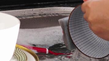 woman is washing tableware in modern kitchen in her apartment, soaping knife. High quality 4k footage video