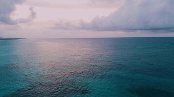 ein atemberaubend Antenne Perspektive von ein Sonnenuntergang Über das Ozean, wo Sanft Rosa Wolken mischen mit Türkis Wasser video
