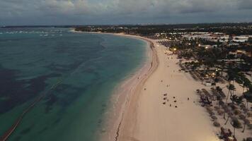 volo al di sopra di il spiaggia di un' popolare turista costiero città a crepuscolo. il città sotto scintille con luci, la creazione di un' mozzafiato spettacolo. punta cana, domenicano repubblica video