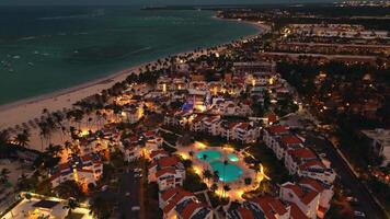 Aerial view of popular tourist coastal city at night. Luxurious tourist hotel with pool illuminated from below. Flickering lights of city below create mesmerizing picture. Punta Cana, Dominican video