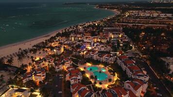 Antenne Aussicht von Beliebt Tourist Küsten Stadt beim Nacht. luxuriös Tourist Hotel mit Schwimmbad beleuchtet von unter. flackern Beleuchtung von Stadt unten erstellen faszinierend Bild. punta Kana, dominikanisch video