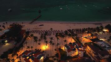 aéreo ver de popular turista costero noche ciudad. un lujo turista hotel con piscina iluminado por luces. el centelleo luces de ciudad abajo crear fascinante fotografía. punta cana, dominicano república video