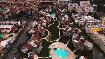 An aerial twilight view of a popular tourist city by the coast. A luxury hotel with a lit-up pool is the focal point, surrounded by sparkling city lights below. This is Punta Cana, Dominican Republic video