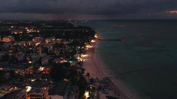 uma deslumbrante aéreo visualizar, ocupado com uma drone, revela uma costeiro cidade às crepúsculo. a cintilante cidade luzes abaixo Formato uma cativante visão. popular turista destino dominicano república, punta cana video