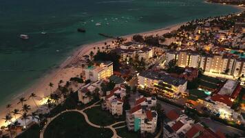 Breathtaking drone aerial perspective showcases coastal city as night falls. Cityscape sparkles with radiant lights, creating mesmerizing scene in this well-loved tourist spot, Punta Cana, Dominican video