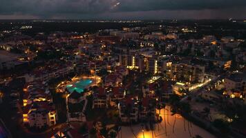 Aerial view of popular tourist coastal night city. A luxury tourist hotel with a illuminated pool. The sparkling lights of the city below create a mesmerizing scene. Punta Cana, Dominican Republic video