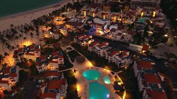 Antenne Aussicht von Beliebt Tourist Küsten Stadt beim Nacht. ein luxuriös Tourist Hotel mit ein beleuchtet Schwimmbad. das flackern Stadt Beleuchtung unten erstellen ein faszinierend Sicht. punta Kana, dominikanisch Republik video