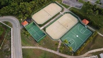 un De arriba hacia abajo ver de Deportes comodidades exhibiendo baloncesto y tenis tribunales, con personas activamente participativo en un vibrante tenis fósforo. esta escena es a el misterios real playa punta cana hotel video