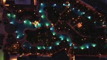 ein Antenne Aussicht beim Nacht erfasst ein Tourist Hotel, ein glühend Schwimmbad, und ein Park mit üppig Bäume, alle einstellen gegen das Hintergrund von Träume königlich Strand im punta Kana, dominikanisch Republik video