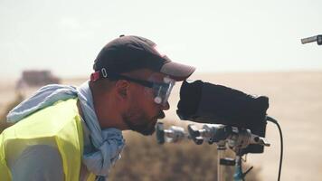 een cameraman in een reflecterende hesje is aan het kijken de het schieten in de woestijn. film schieten.vrachtwagens voorbijgaan door video