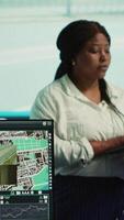 Vertical African american manager guiding her team to monitor surveillance footage on a big screen, observing traffic flow in the city. Government agency operating CCTV satellite system. Camera A. video