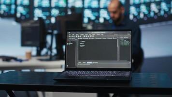 Focus on laptop used by technician in blurry background programming in data center room housing servers. Close up shot of code lines on notebook display in data storage facility video