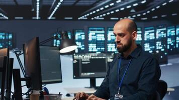 System operator overseeing server room, typing code on desktop PC, troubleshooting rigs. Software specialist doing maintenance on hardware clusters, networking systems and storage arrays video