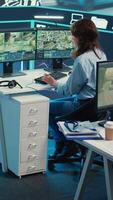 vertical supervisión habitación operador mirando para rutas en vigilancia imágenes y GPS satélite mapa, estrella de guía mensajero a evitar tráfico. mujer agencia empleado operando con cctv sistema. cámara b. video