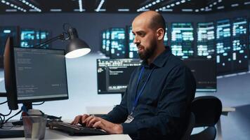 Engineer coding, working in network security data center facility hosting supercomputers, ensuring optimal performance. IT expert using desktop PC to monitor energy consumption across server cabinets video