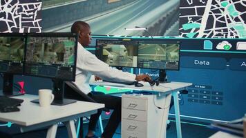 Operator uses satellite navigation map to guide delivery truck drivers, works in observation room to avoid traffic. African american employee tracing orders within the surveillance system. Camera B. video