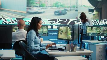 Indian woman operator locating delivery truck and offers gps coordinates of the shipment location. Control center employee consults satellite map and CCTV system for routes. Camera B. video