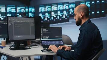 Man in server room typing code on laptop and PC, ensuring data remains shielded from threats. IT expert using notebook and computer to protect supercomputers against unauthorized access video