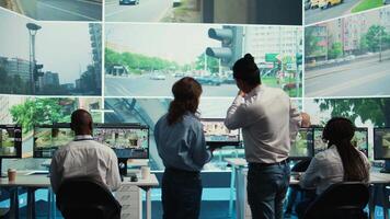 Diverse team following city traffic on a display in monitoring room, reviewing CCTV satellite radar footage. Employees working on surveillance and data collecting, control center. Camera B. video