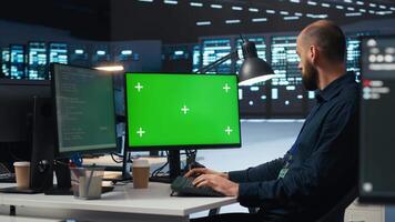 Man typing code on green screen computer in high tech data center with server rows providing computing resources. IT specialist using mockup PC to oversee rackmounts operating data video