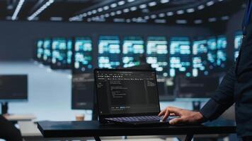 IT support employee writing code on laptop in high tech facility with server rows providing computing resources for different workloads. System administrator uses notebook to oversee supercomputers video