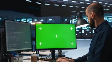 System administrator working on green screen computers in data center, ensuring optimal performance. Worker monitoring energy consumption across servers with mockup PC displays video