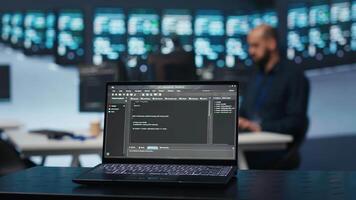 Focus on script running on laptop in server room with man in blurry background safeguarding data from threats. Close up shot of lines of code on notebook written by expert protecting supercomputers video